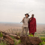 Ruedi und ein Massai stehen nebeneinander. Der Massai hält seinen Speer und Ruedi seinen Filmstick