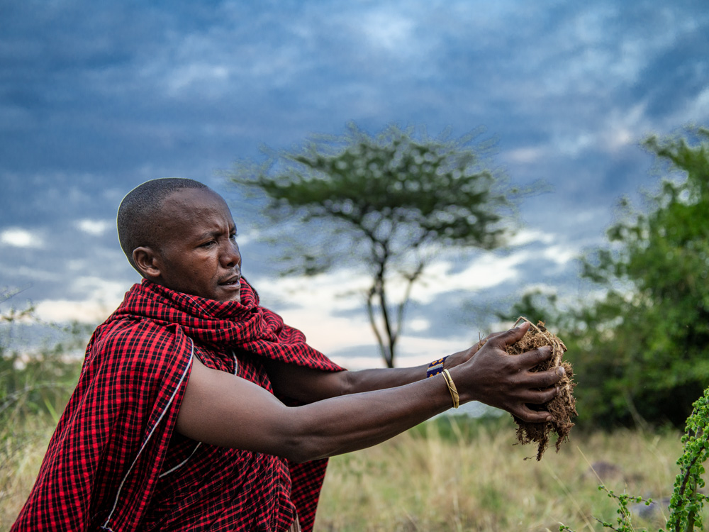 Der Massai hält den Elefantendung in den Wind und entfacht so das Feuer