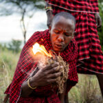 Der Massai bläst ins einen Elefantendung und entfacht so das Feuer