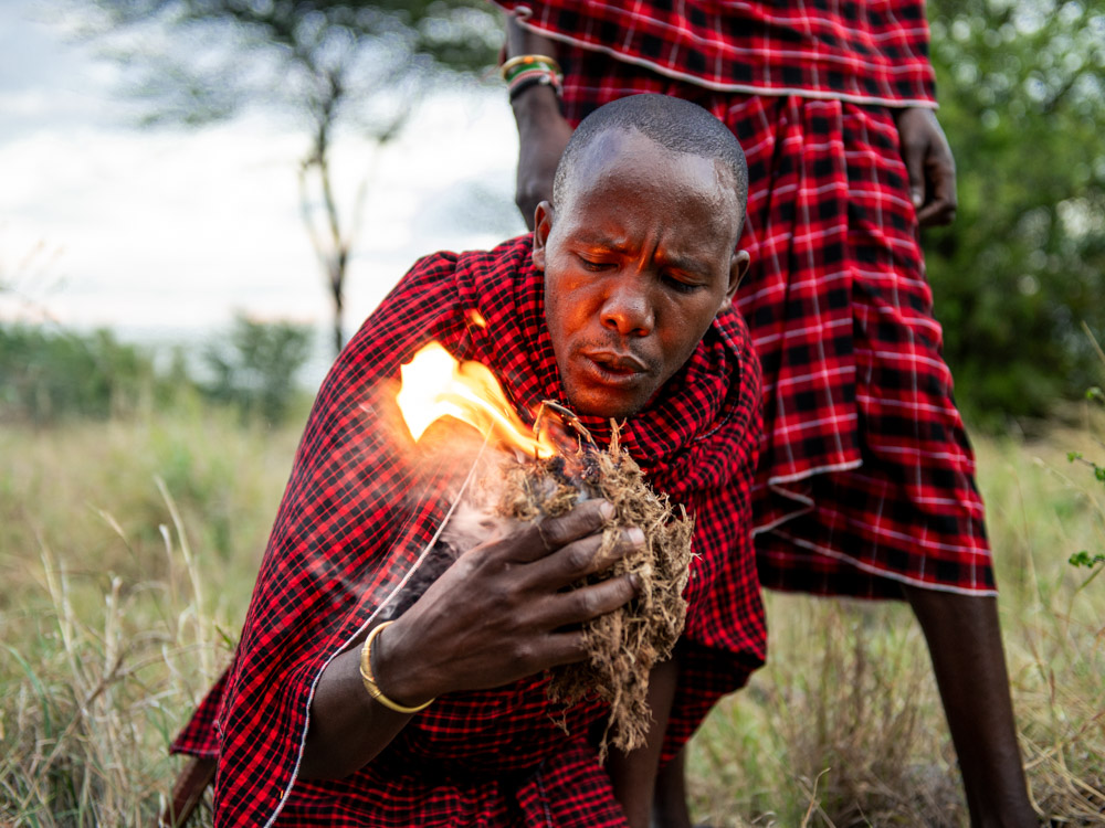 Der Massai bläst ins einen Elefantendung und entfacht so das Feuer