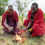 Massai wärmen sich am eben entfachten Feuer die Hände