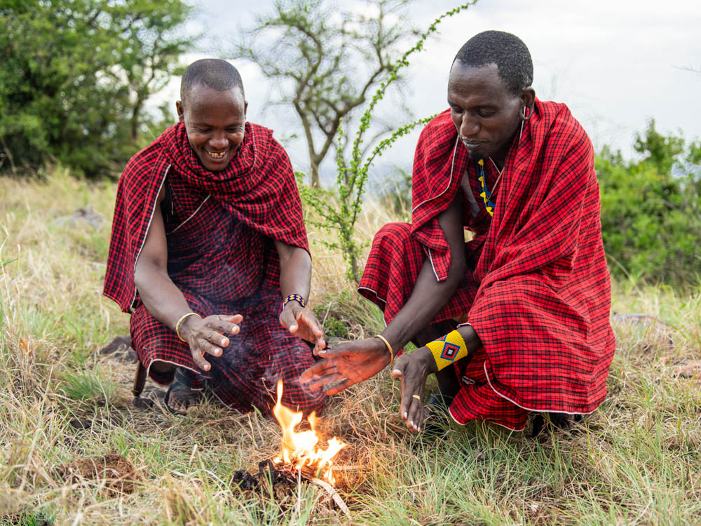 Massai wärmen sich am eben entfachten Feuer die Hände
